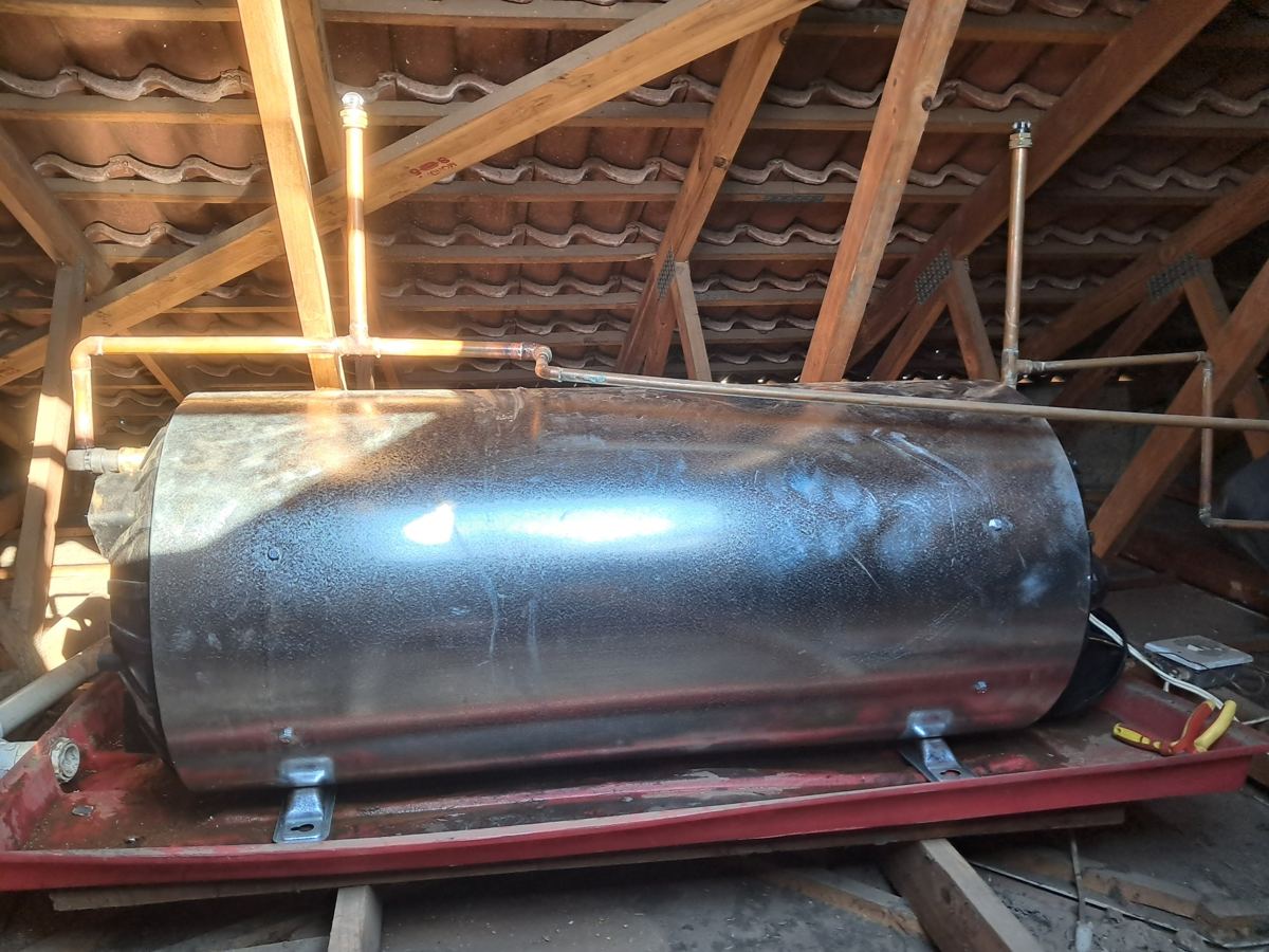 New 150 litre horizontal geyser on a drip tray in a roof space, with copper pipework and vacuum breakers on both sides